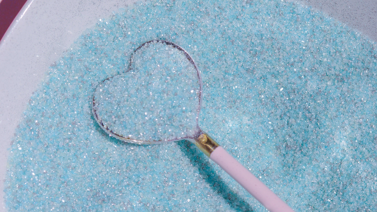 Blue sugar with a heart-shaped spoon on a pink background